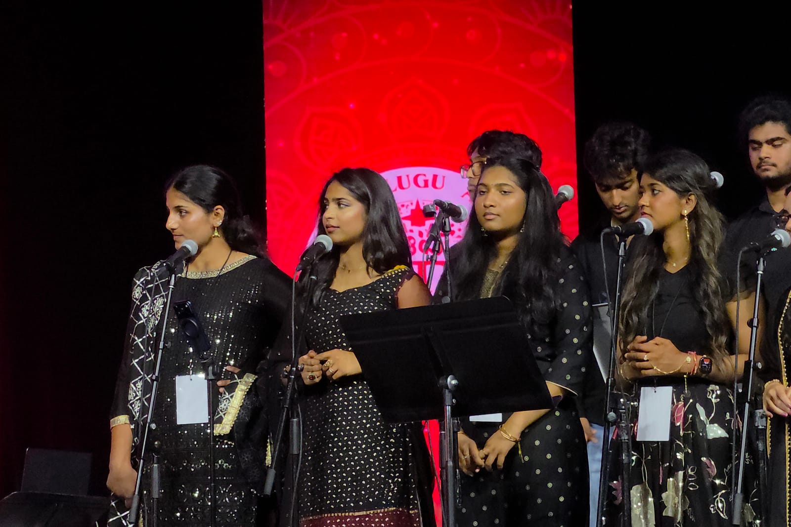 The vocal ensemble lined up across the stage against a red backdrop.
