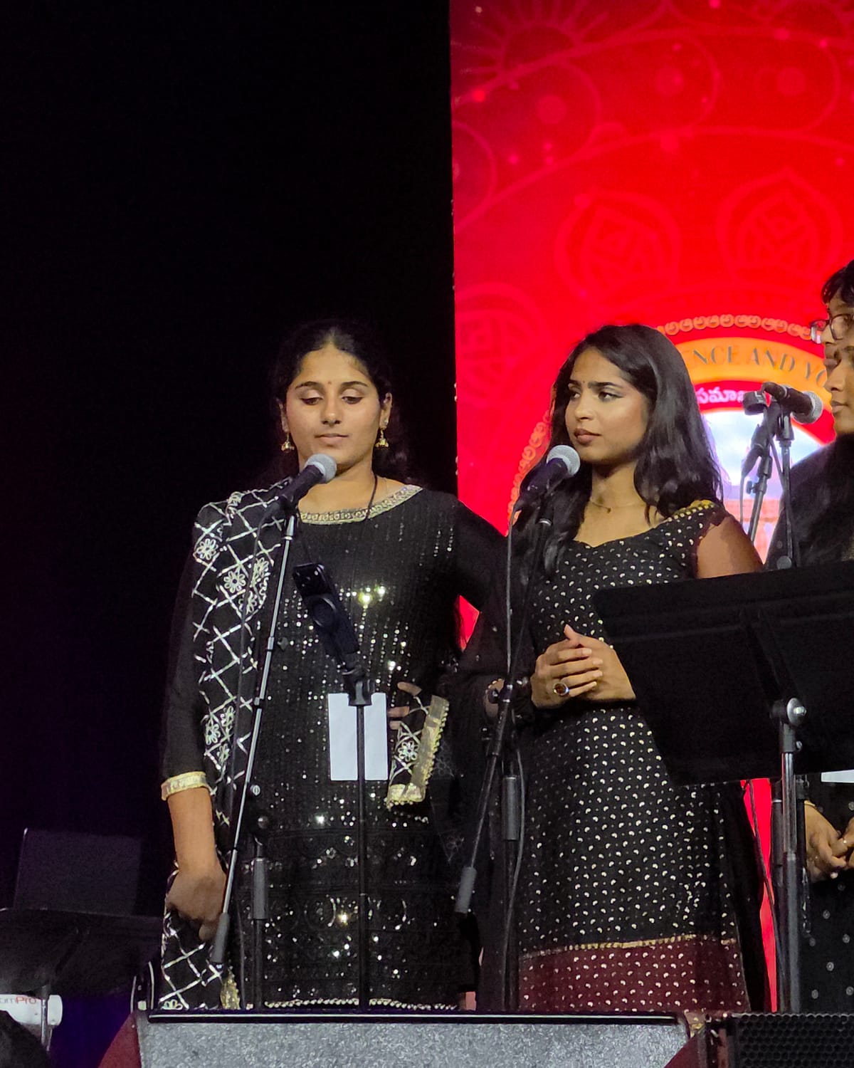 Singers at their microphones mid-performance, music stands in front of them.