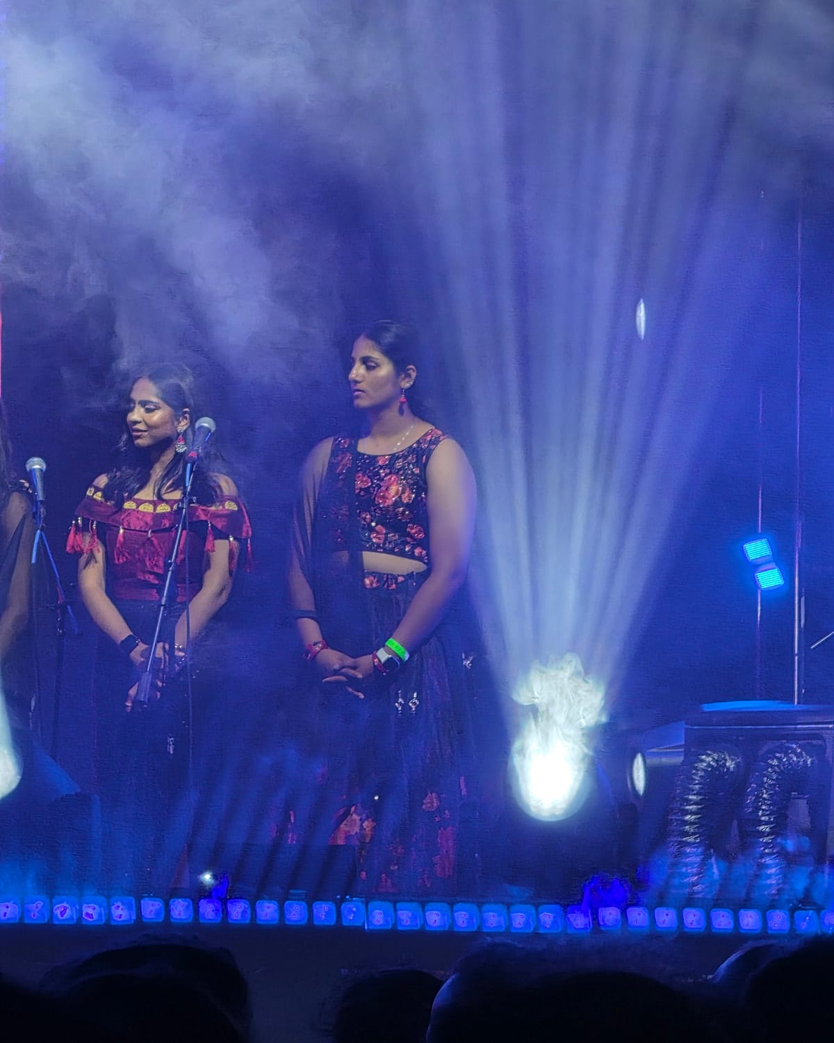 Hasitha on stage in heavy haze, blue beams fanning out behind her.